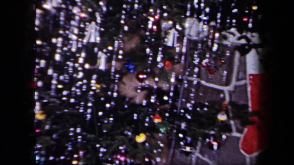 1958 New York home-movie view of a Christmas tree with silver tinsel, glowing ornaments, lights, and part of the fireplace.