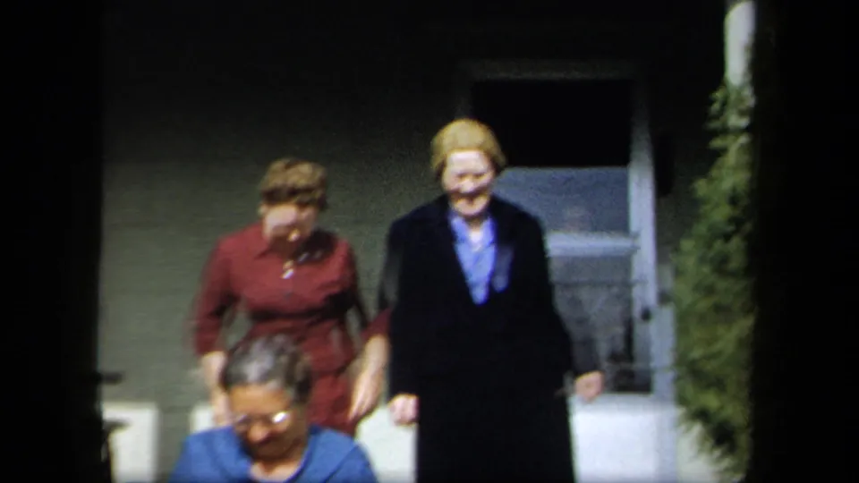 Three adult women walk toward the camera from a residential entrance, including one in a dark coat smiling in the 1958 New York footage.