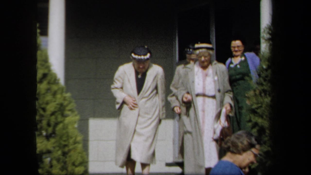 1958 New York frame showing older women in hats and light coats exiting a building, with faces visible.