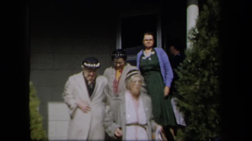 1958 New York home-movie frame of women in formal mid-century clothing leaving a porch and steps.