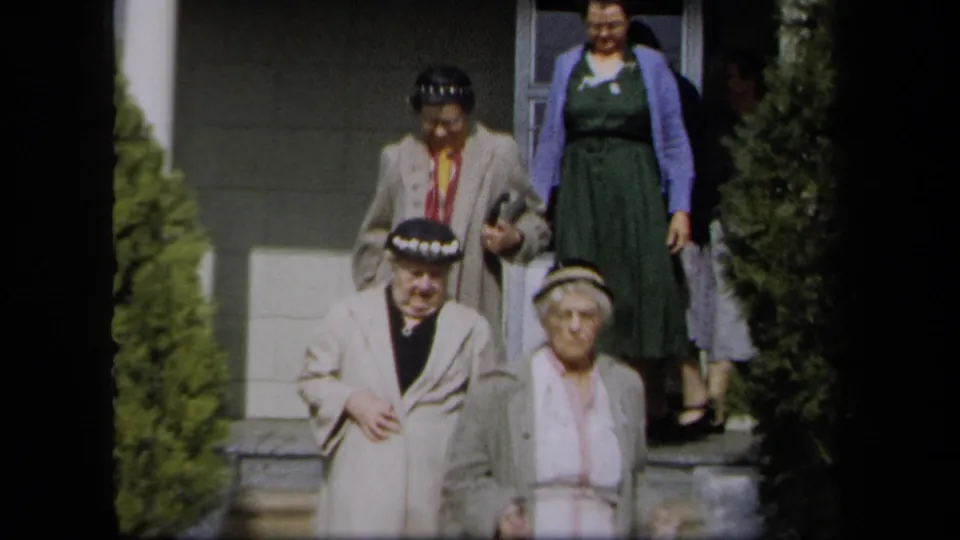 1958 New York frame of women leaving a building, including light coats, hats, dresses, and visible faces.