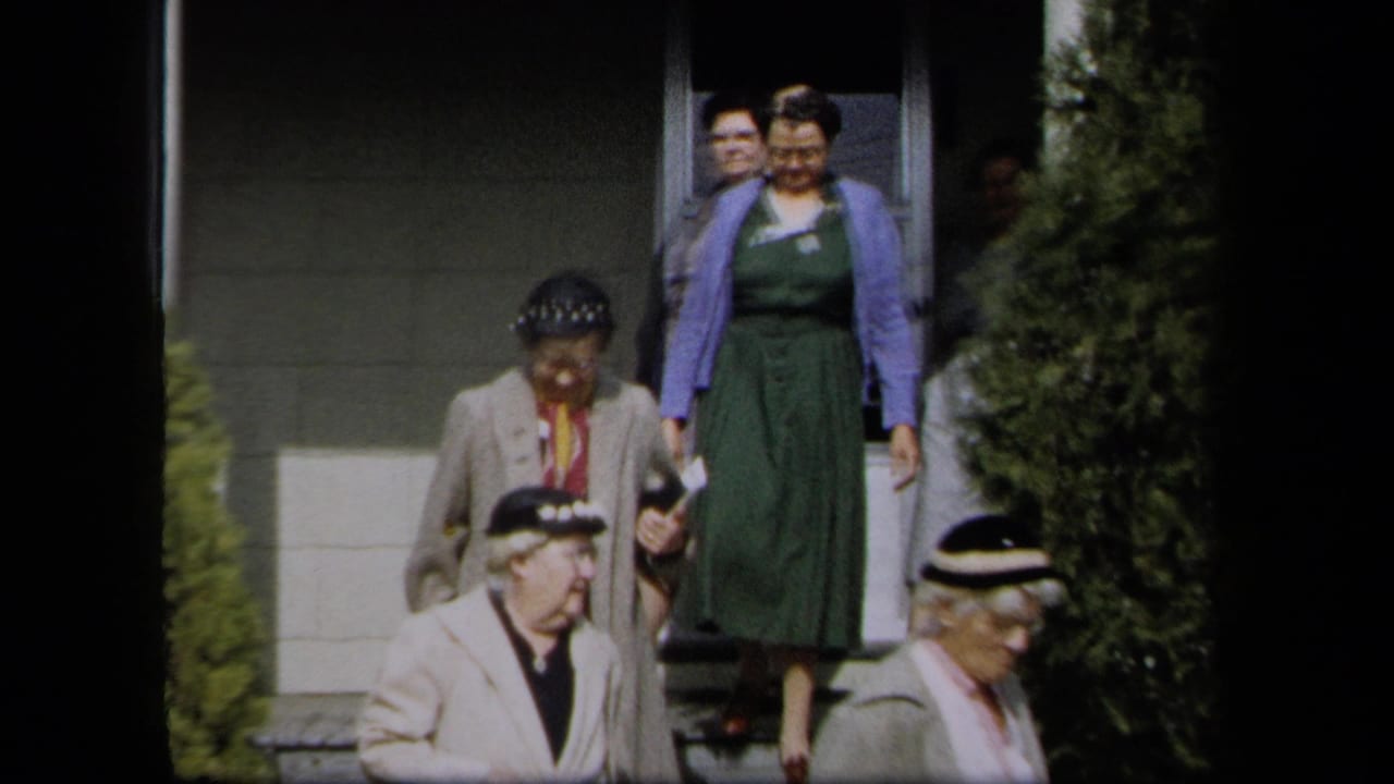 Several women in dresses and cardigans walk down steps outside a house.