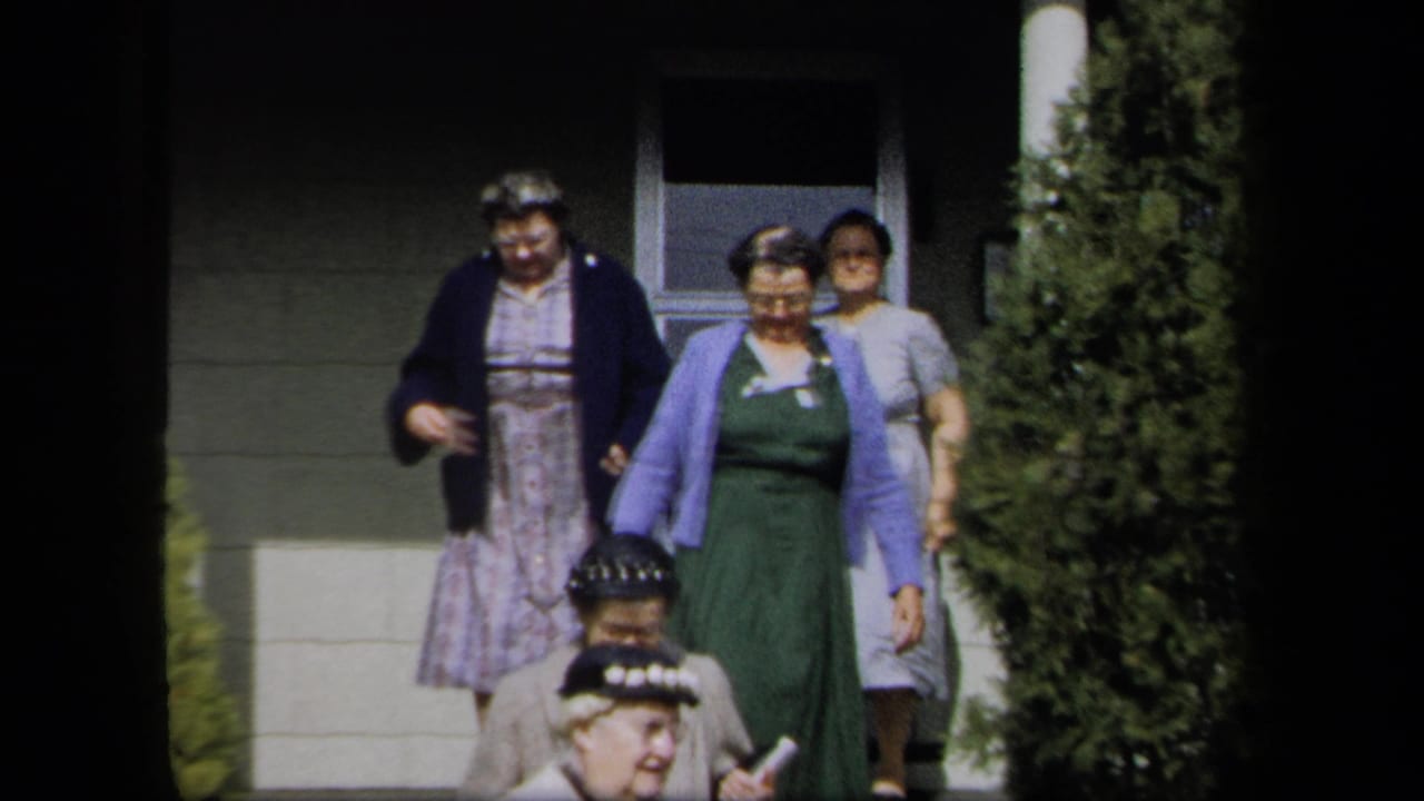 Adult women in 1950s attire move outside a New York residence, with a doorway, steps, and tall shrubbery visible.