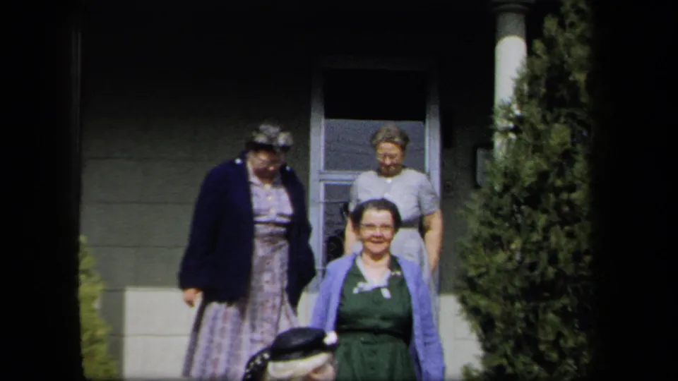 The frame shows adult women walking down exterior steps, with mid-century clothing and a residential doorway behind them.