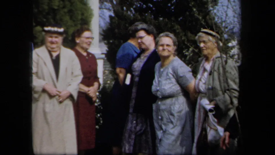 Adult women in mid-century clothing stand outside a New York residence, some smiling and others turning aside.