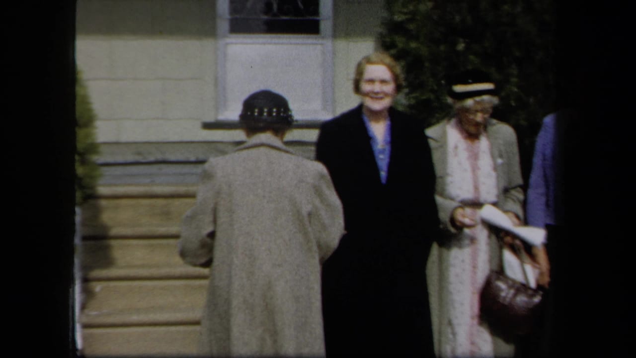 1958 New York home-movie frame of women standing outside a house, with a woman in a dark hat seen from behind.