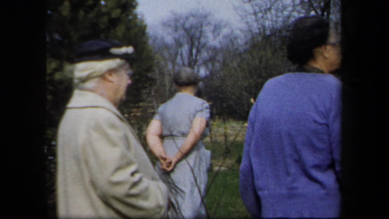 1958 New York 8mm frame of adults, mostly women, walking away through a cool-season garden with leafless trees.