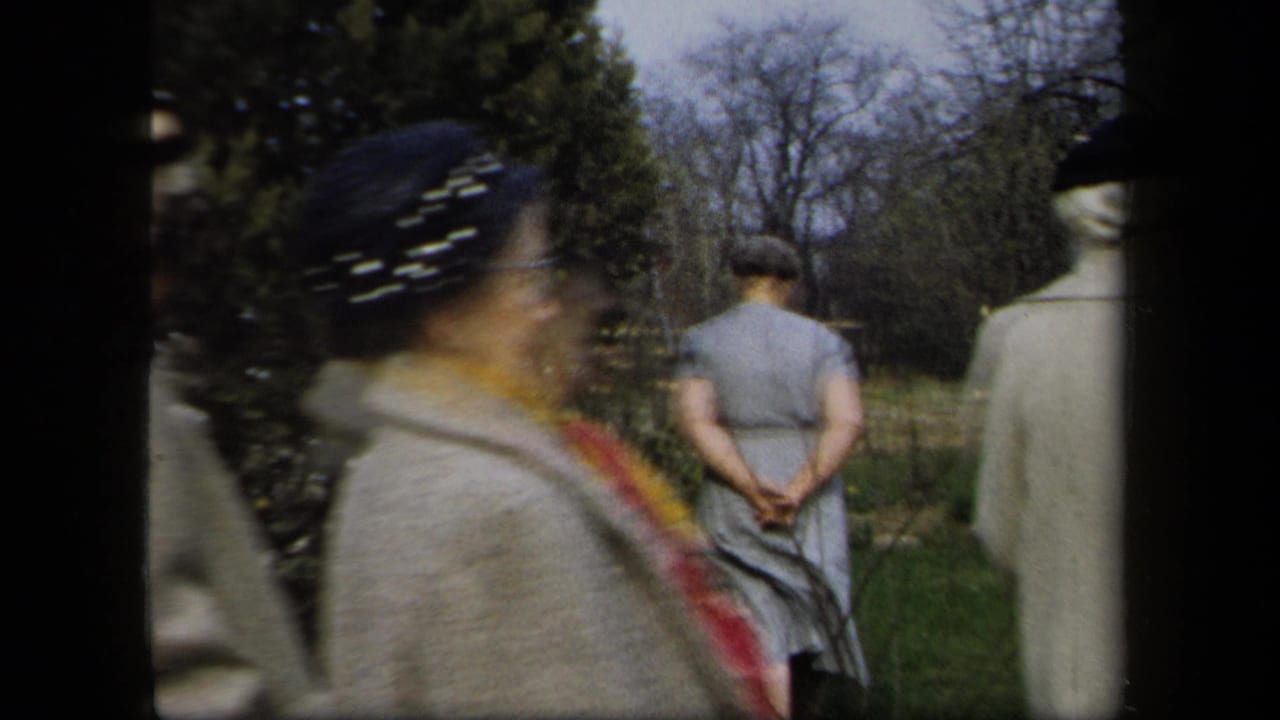 Blurred woman in hat and scarf passes in front of others walking in a garden.