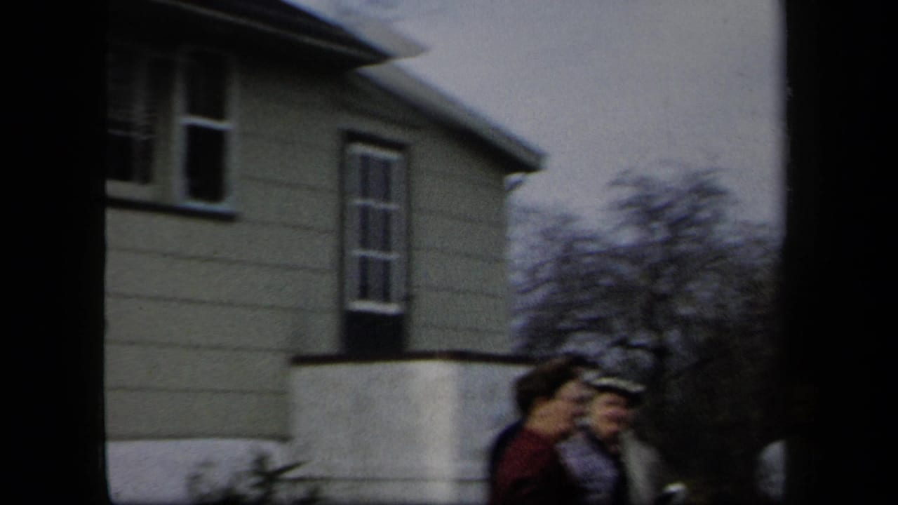 A residential house and several adult women are visible in an outdoor New York home-movie frame from the 1958 clip.