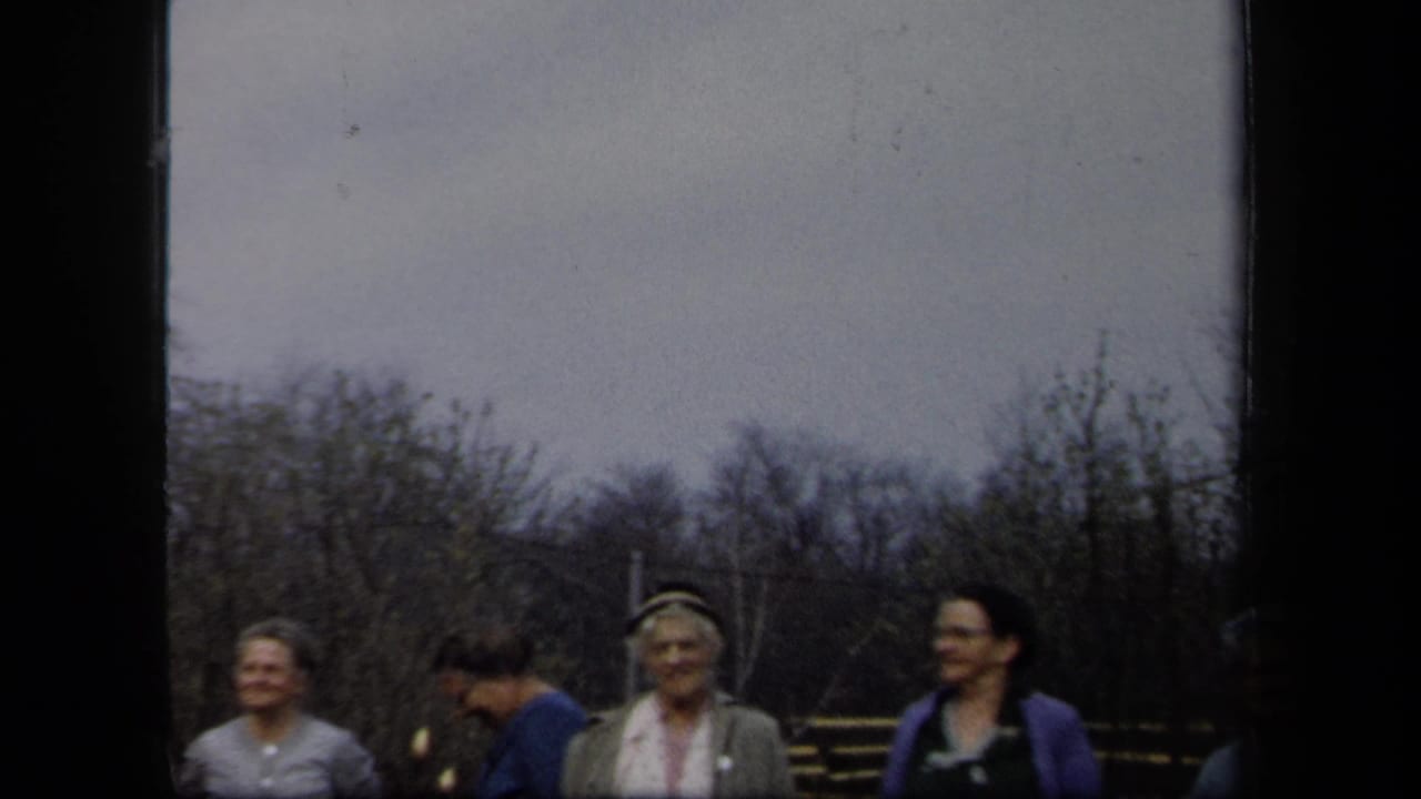Adult women in late-1950s clothing stand outdoors in New York, with hats, sweaters, bare trees, and a dark vertical film edge visible.