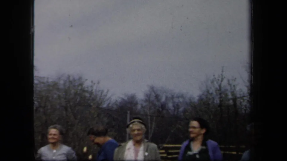 Adult women in late-1950s clothing stand outdoors in New York, with hats, sweaters, bare trees, and a dark vertical film edge visible.