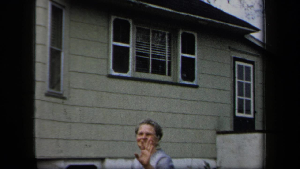 Adult woman smiles toward the camera outside a light-sided house in metadata-supported 1958 New York home-movie footage.
