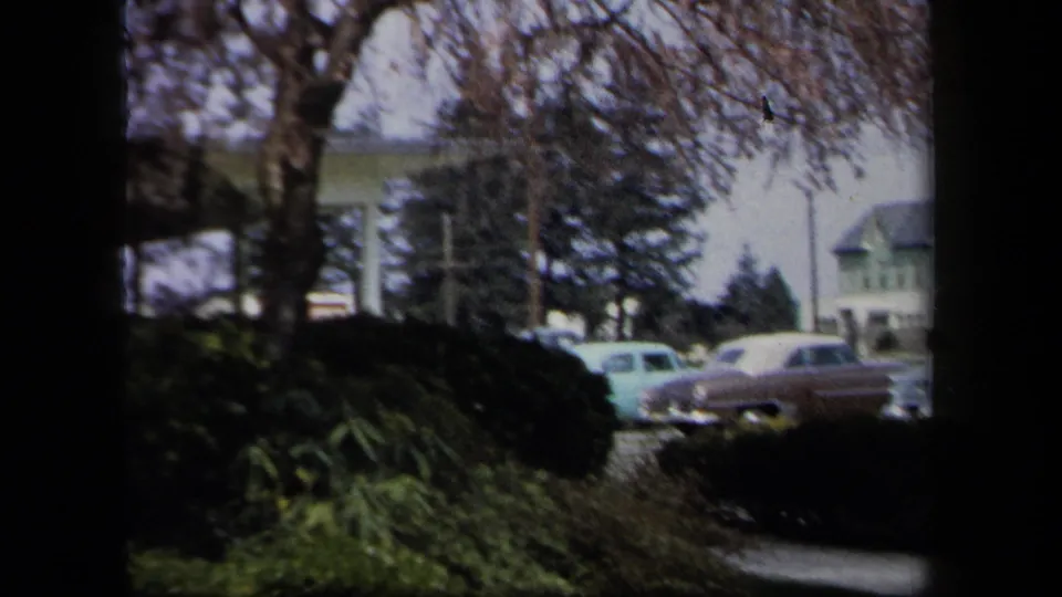 Suburban street view with shrubs, houses, and several vintage cars in metadata-supported 1958 New York footage.