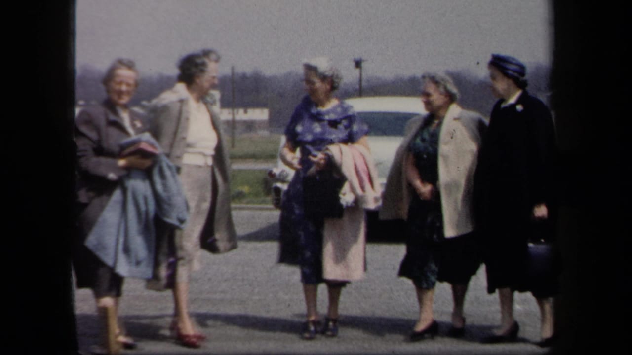 Five adult women in coats, dresses, hats, and handbags chat in a New York parking lot, consistent with 1958 metadata.
