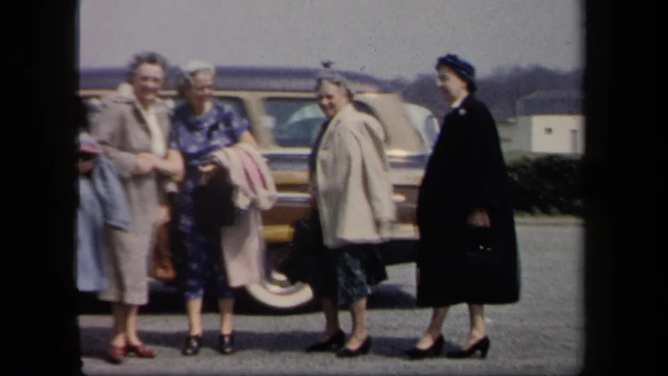Four adult women in 1950s-style clothing stand in a parking lot with parked cars behind them, based on the 1958 metadata.