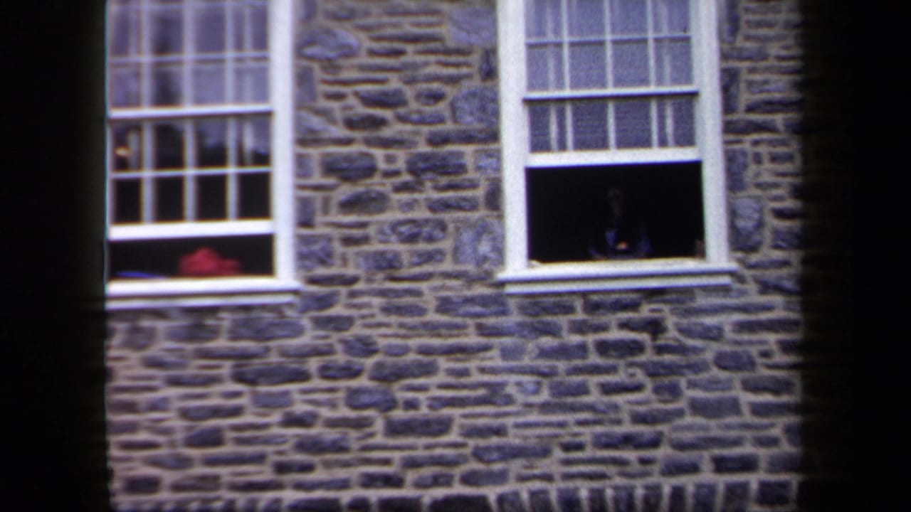 1958 New York home-movie frame showing a stone building facade with white sash windows and one open lower window.