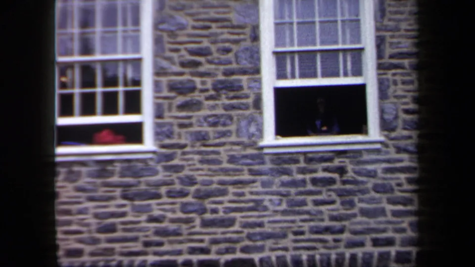 1958 New York home-movie frame showing a stone building facade with white sash windows and one open lower window.