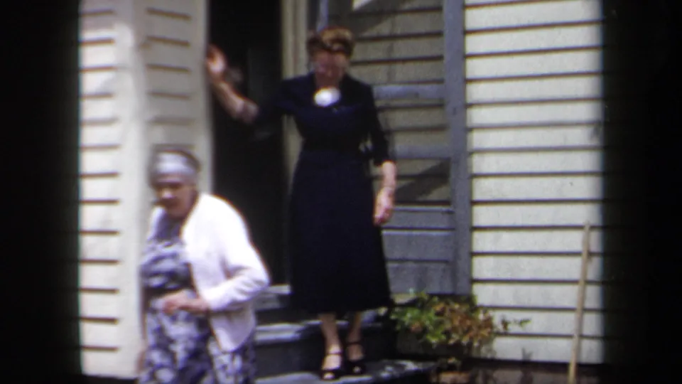 1958 New York frame with a dark-dressed woman standing on the step and an elderly woman in a floral dress moving across the foreground.