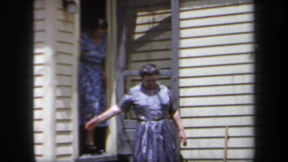 1958 New York home-movie frame of a woman gesturing from a porch area as another woman remains in the doorway.