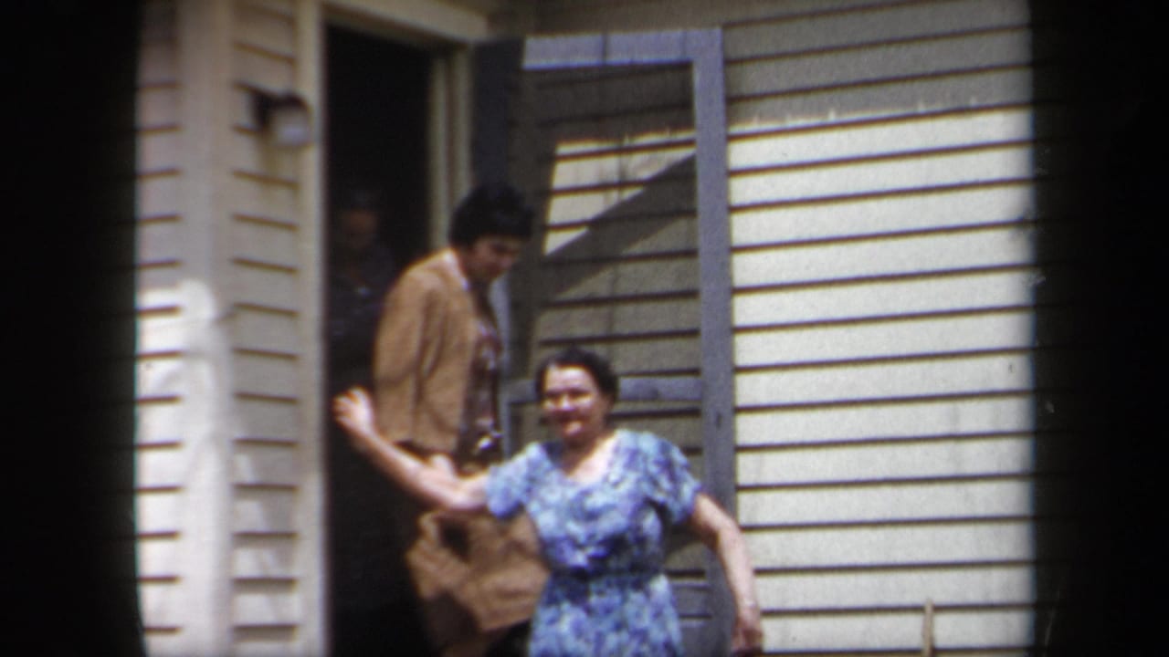 A woman in a blue dress smiles near the doorway while another person stands behind her.