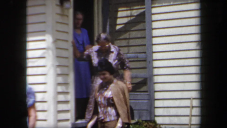 Several women cluster at the entrance of a New York house, with one stepping out and others visible behind her.