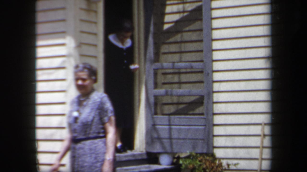 Woman in a patterned dress walks past a doorway as another woman stands behind her.