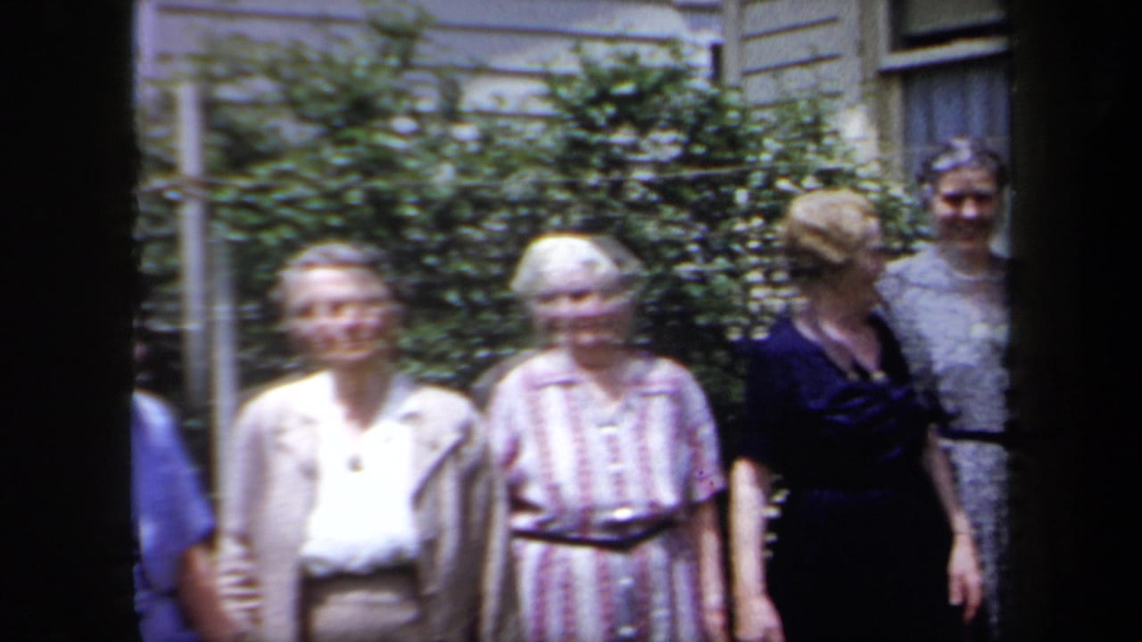 Older women pose together outside a New York residential house in 1958, with shrubs and clapboard siding behind them.