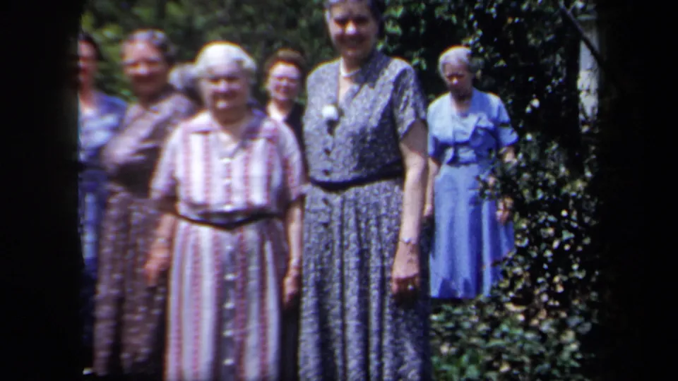 Women in 1950s-style dresses stand outdoors, with a striped pink dress and dark patterned dress prominent in the frame.