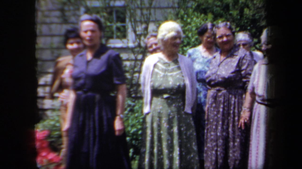 Older women in 1950s dresses and cardigans stand in a New York garden, with red flowers and leafy plants behind them.