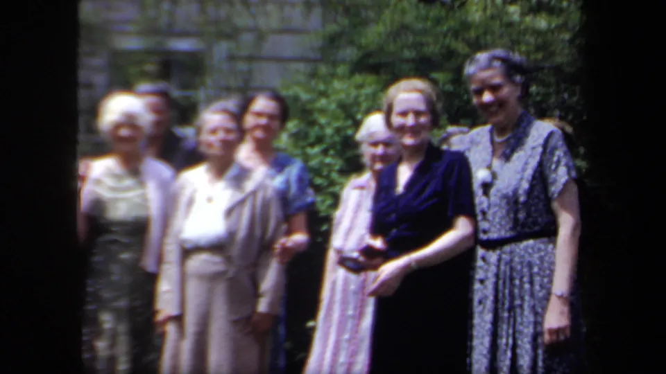 In 1958 New York home-movie footage, older women in dresses gather in a garden and look toward the camera.