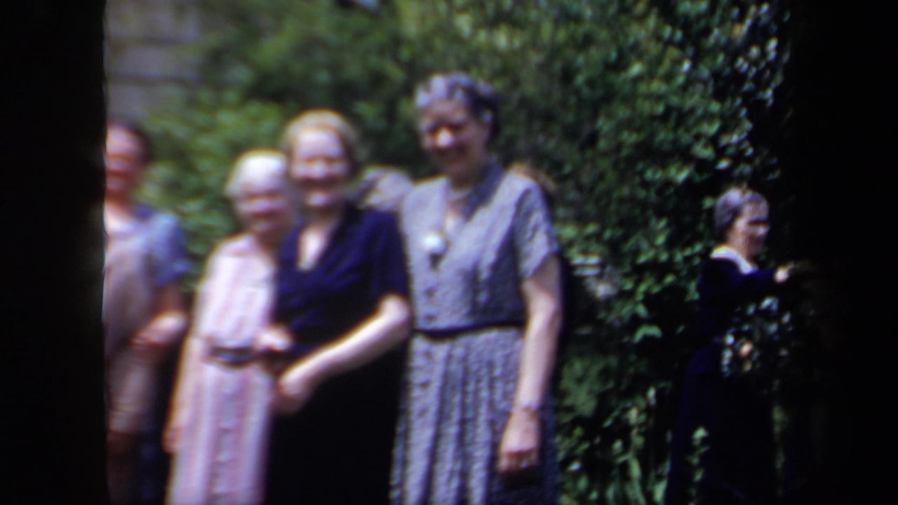 Several older women smile in a garden, with another person partly visible at the right edge.
