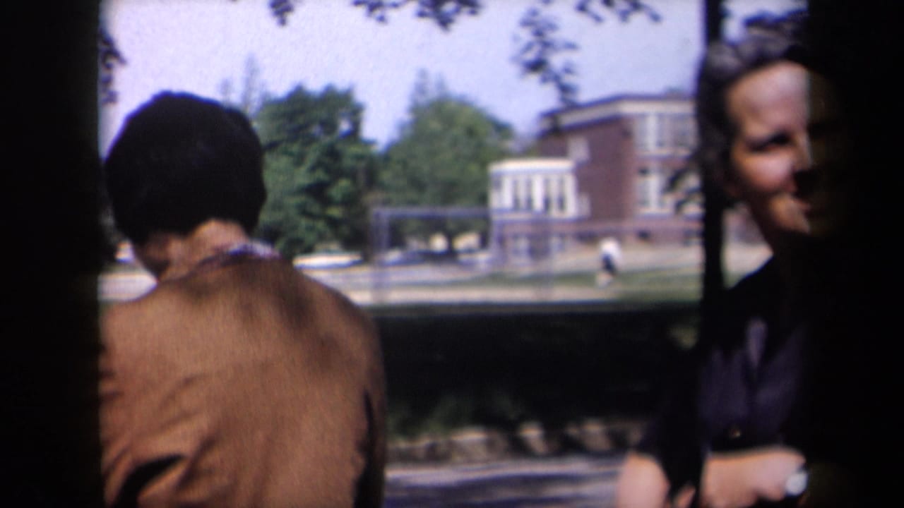 Woman seen from behind near a street while another adult stands at the right edge.
