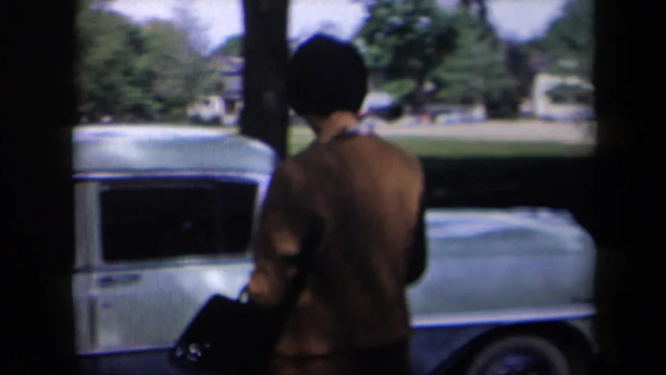 1958 New York street scene showing a woman in a brown jacket beside a light blue sedan under tree shade.