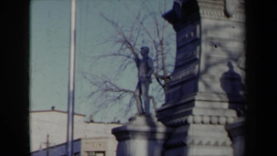The final frame centers higher on the New York monument, showing a statue on a pedestal, winter-bare branches, and surrounding buildings.