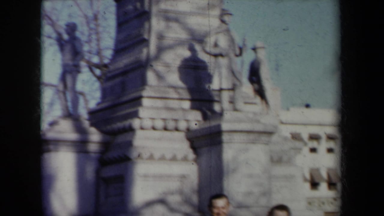 Stone monument base with sculpted figures, pedestal blocks, shadows, and partial faces at the lower edge.