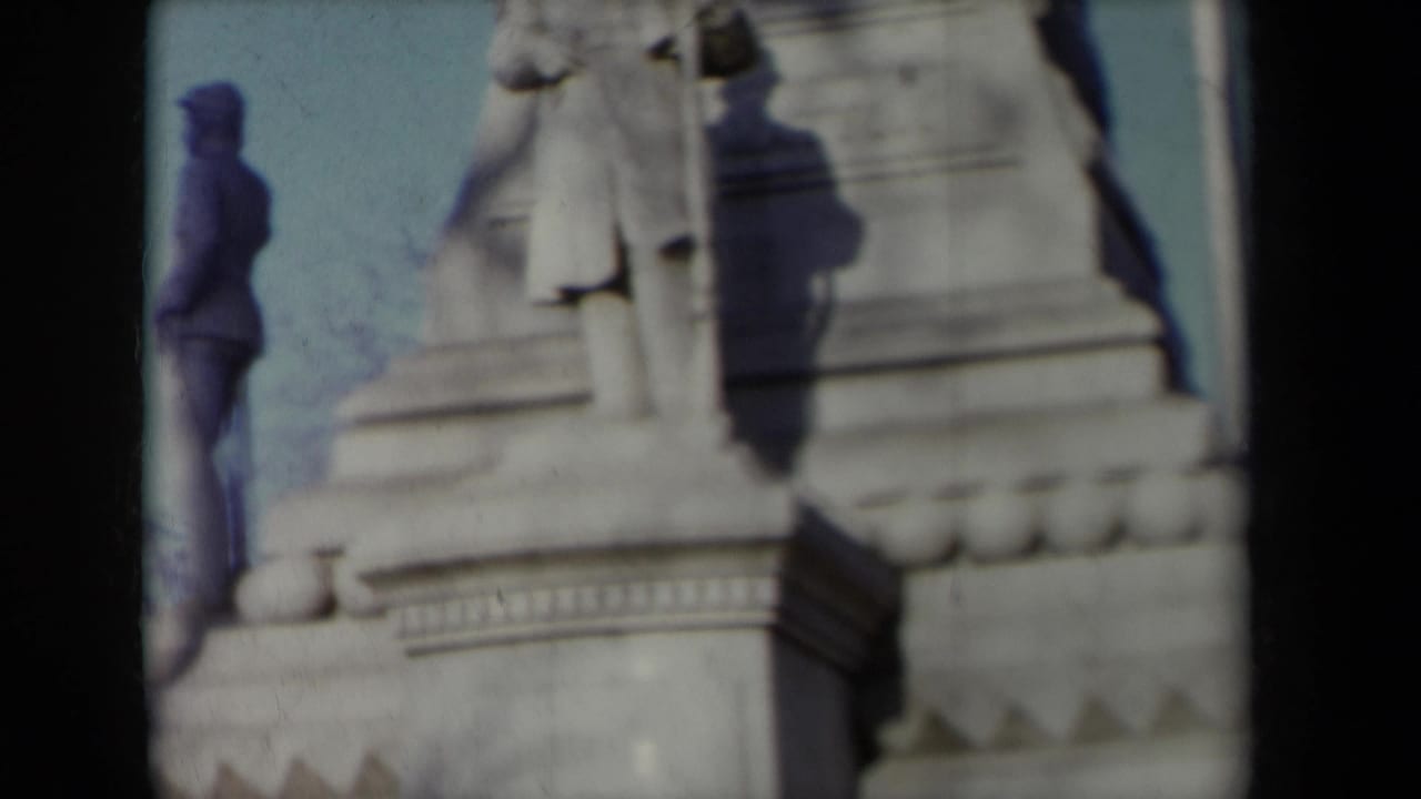 1959 New York 8mm frame showing a stone soldier figure on a Civil War monument, partly cropped and softly focused against blue sky.