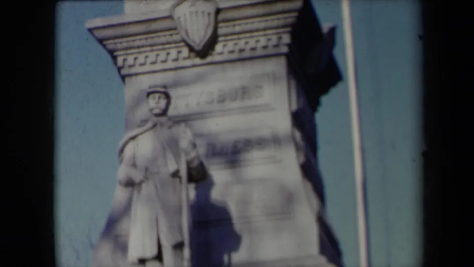 1959 New York 8mm frame showing a closer visitor-shot view of a stone soldier statue, carved monument details, and weathered lettering.