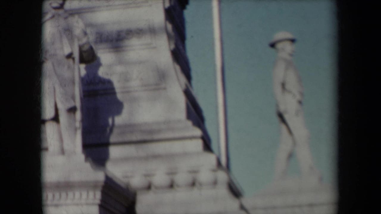 Close view of stone monument base with a standing statue and blue sky.