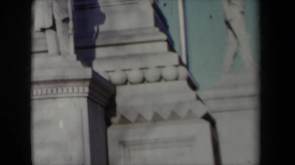 Close 8mm frame of a carved stone pedestal and partial standing figure, filmed from below in New York in 1959.