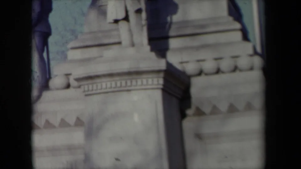 1959 New York frame showing lower portions of monument statues and a tiered stone pedestal with ornamental detailing.