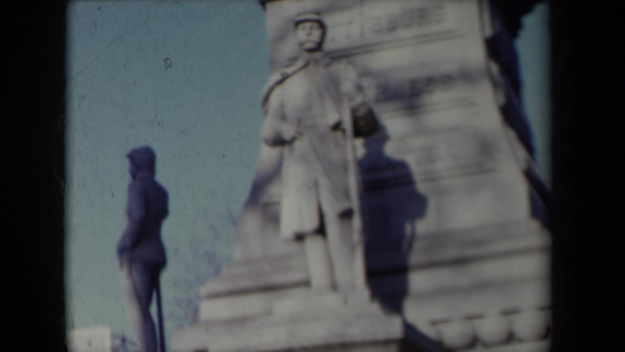 Stone monument or sculpture beside a sidewalk, seen in soft focus with dark film edges.