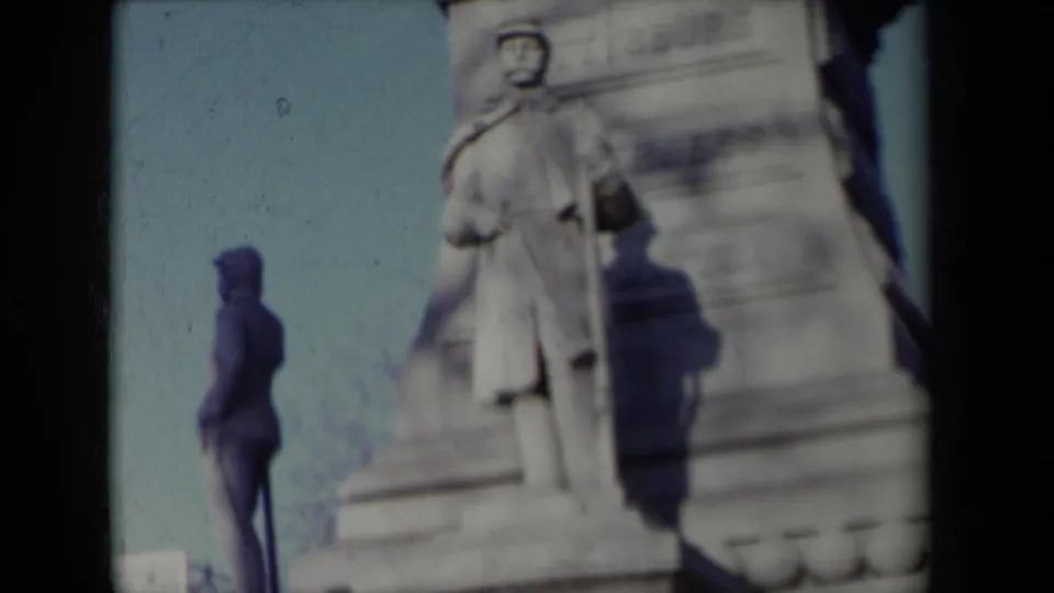1959 New York home-movie frame showing a stone monument or sculpture near a sidewalk, with soft focus and visible film edge shadow.