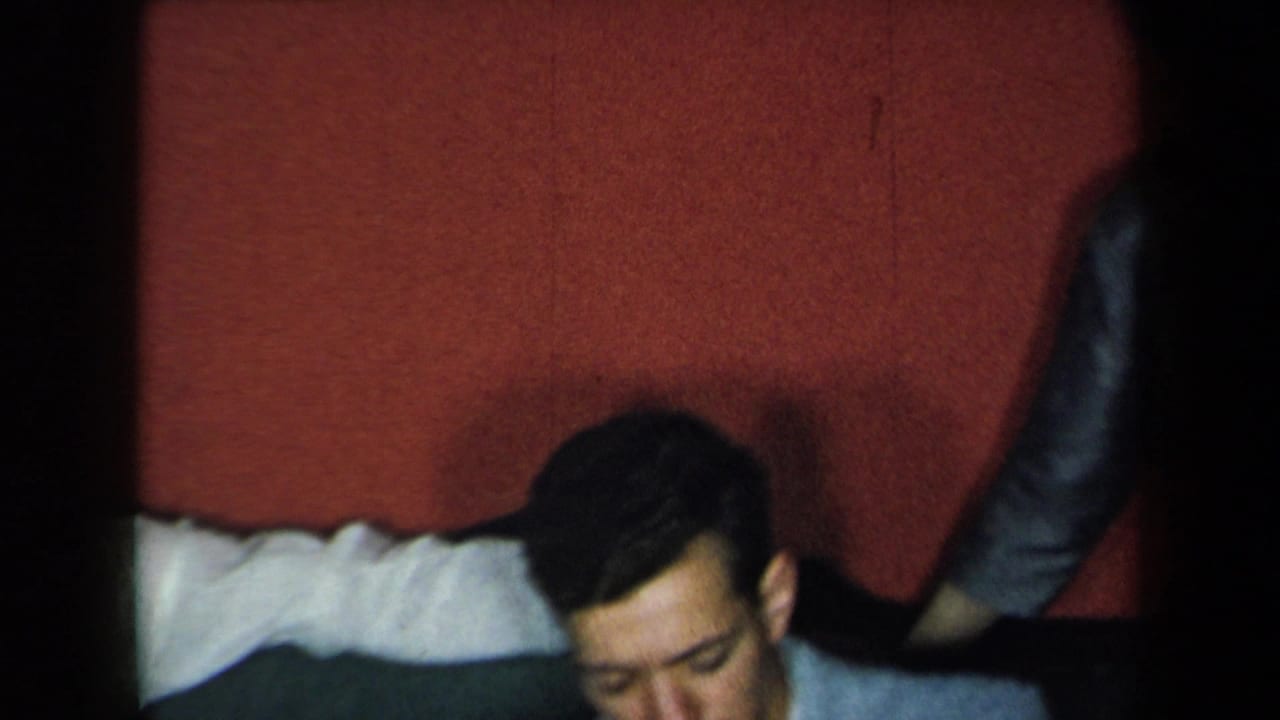 Adults on a couch against a red wall, with one man partly cropped and others partly obscured.
