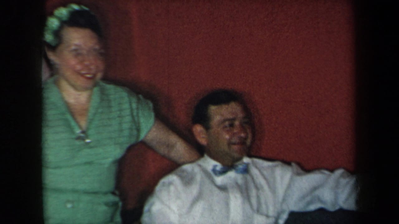 Woman in a green dress stands beside a seated man in a white shirt and bow tie.