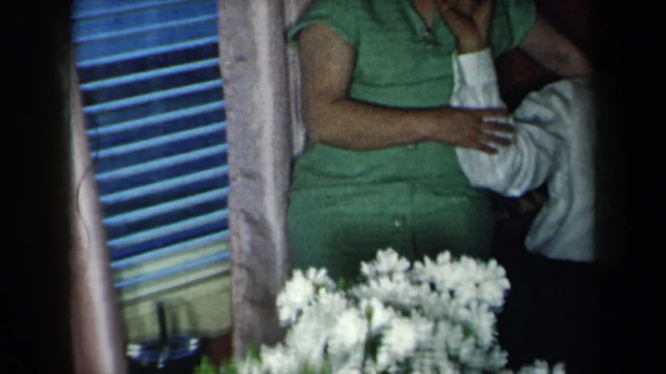 1959 New York home-movie frame showing a playful gesture between a seated man and standing woman in a private interior.