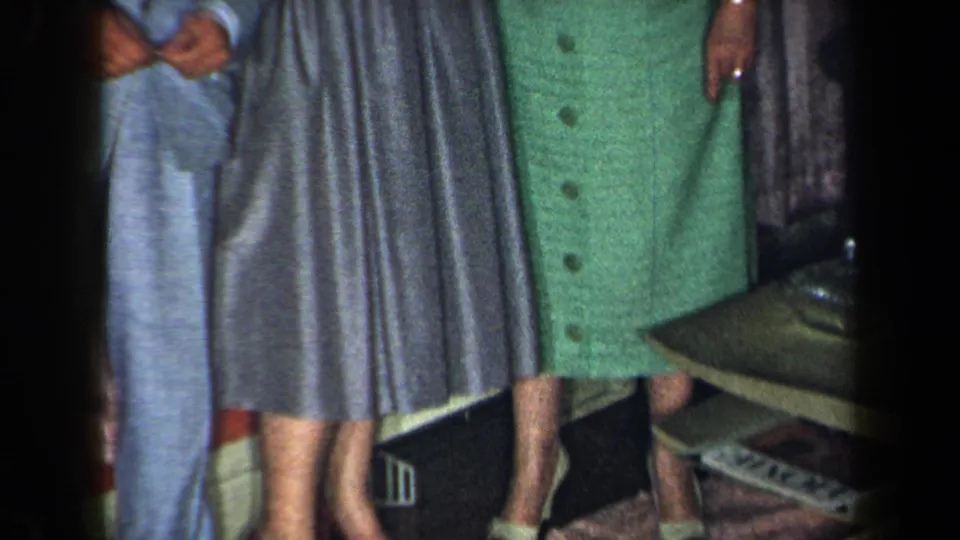 1959 New York home-movie frame focused on lower clothing details, including a blue suit, grey skirt, green dress, and heels.