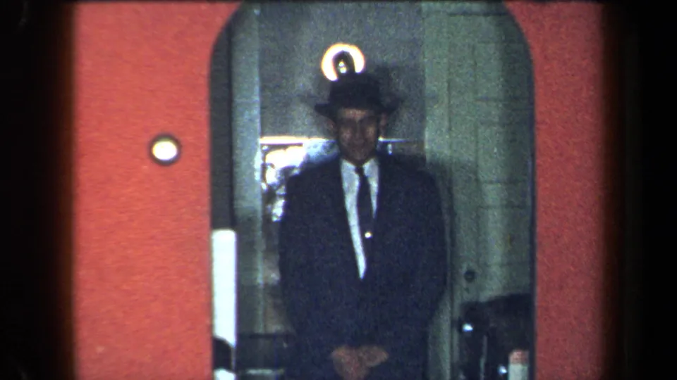A man in a dark suit, tie and brimmed hat appears in a New York private interior doorway in this 1959 8mm home-movie frame.