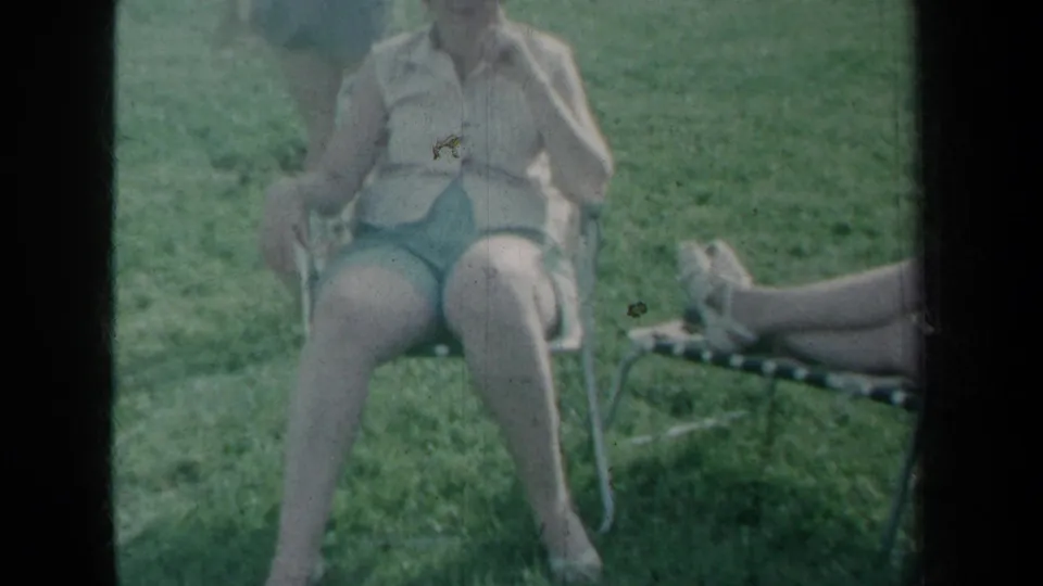 1959 New York yard scene showing a woman in shorts seated on a metal chair, with lounge chair legs visible at right.