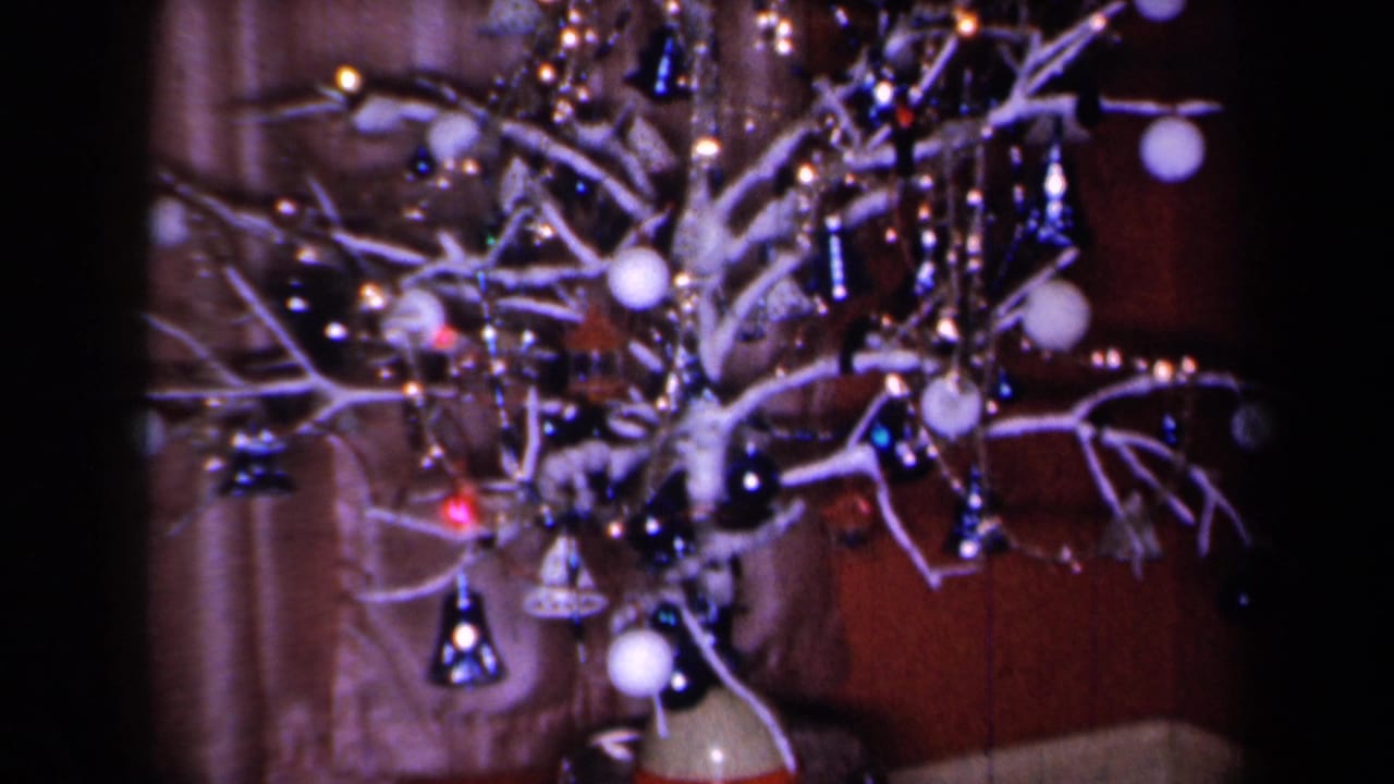 1959 New York home-movie frame showing a small decorated Christmas tree with ornaments near a poinsettia on a cabinet.