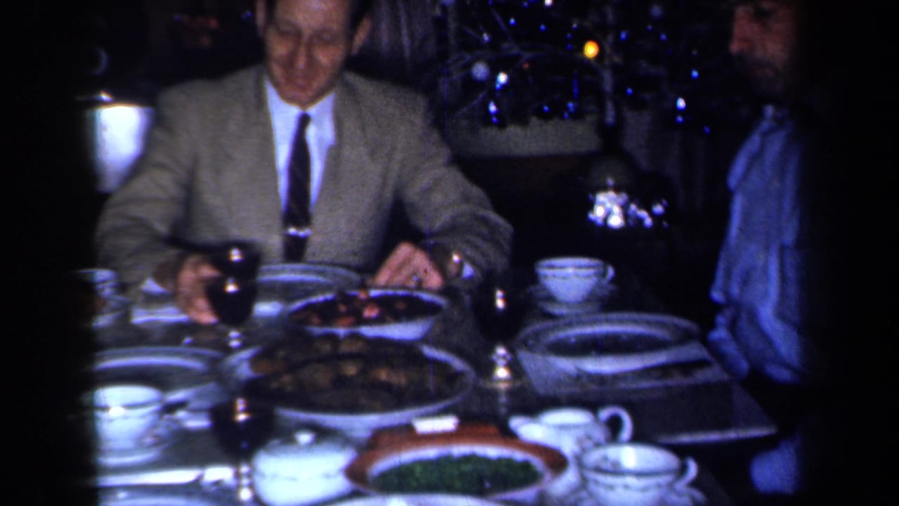 Man in a suit seated at a formal dinner table with plates, cups, and serving dishes.